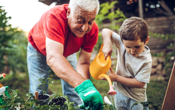 A grandfather helping his young grandson water plants outside