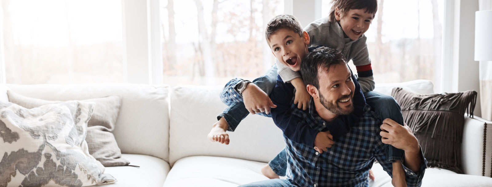 A dad holding up two young boys over a couch