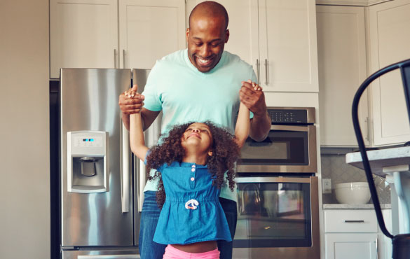 A dad holding his young daughters hands in a modern kitchen
