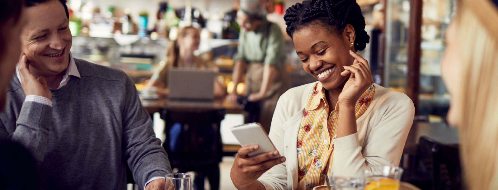 A woman holding a smartphone at a cafe with friends